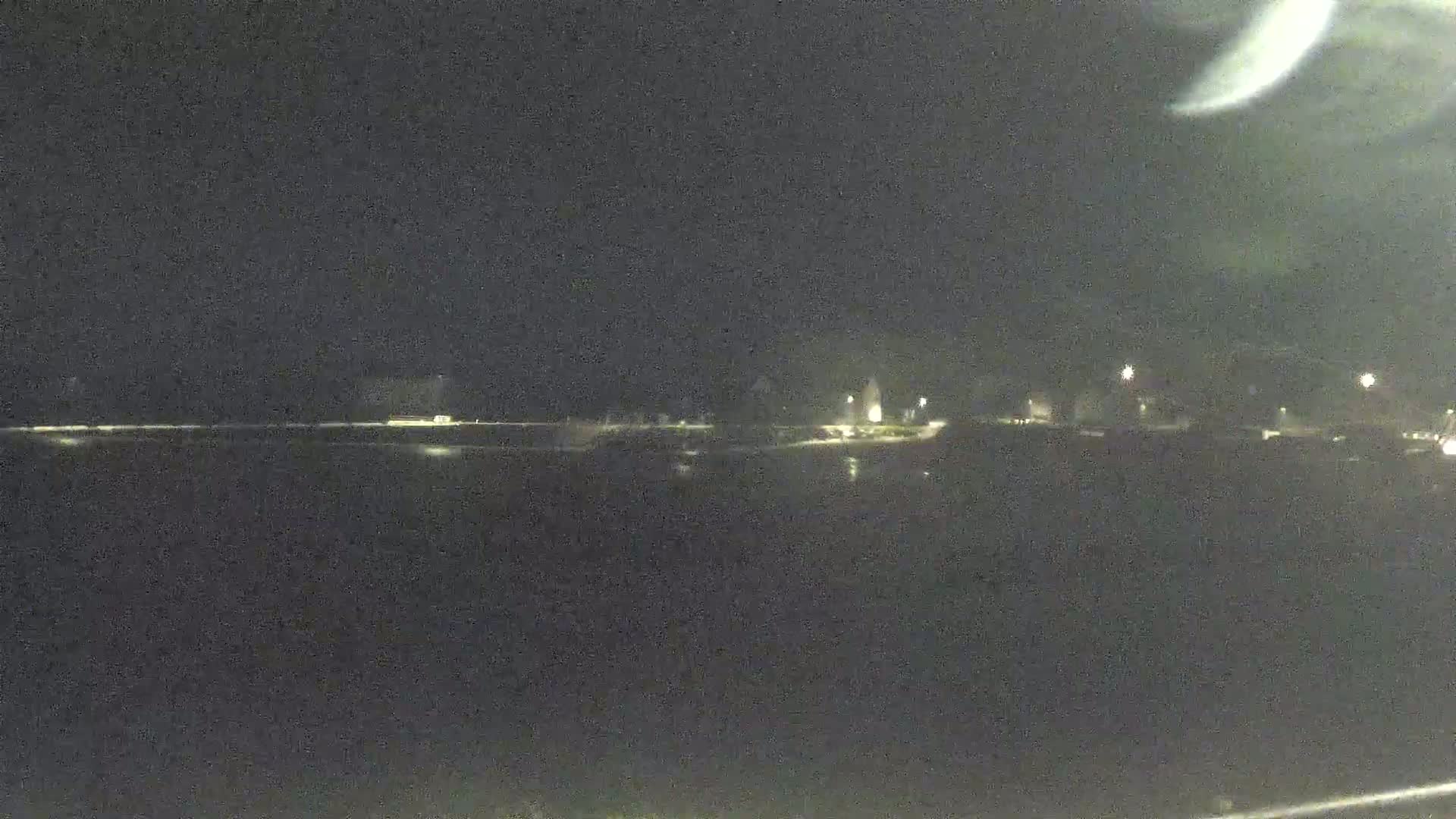 A dark, nighttime view shows a body of water reflecting the faint lights of a distant shoreline.