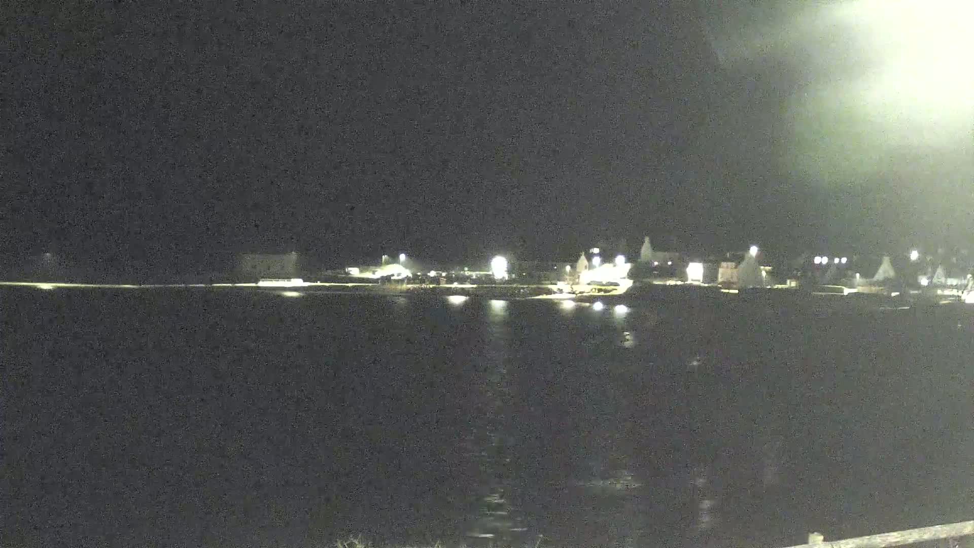 A nighttime view of a dark body of water with a dimly lit shoreline featuring several structures.