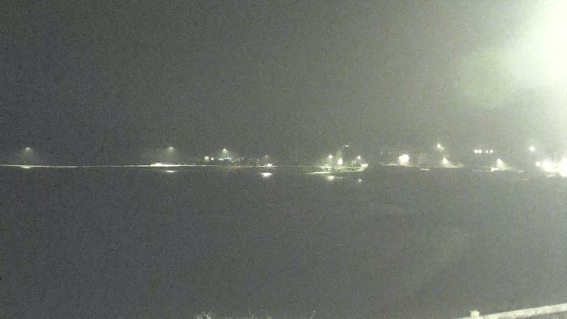 A nighttime, hazy view shows a dark body of water reflecting the faint lights of a distant shoreline.