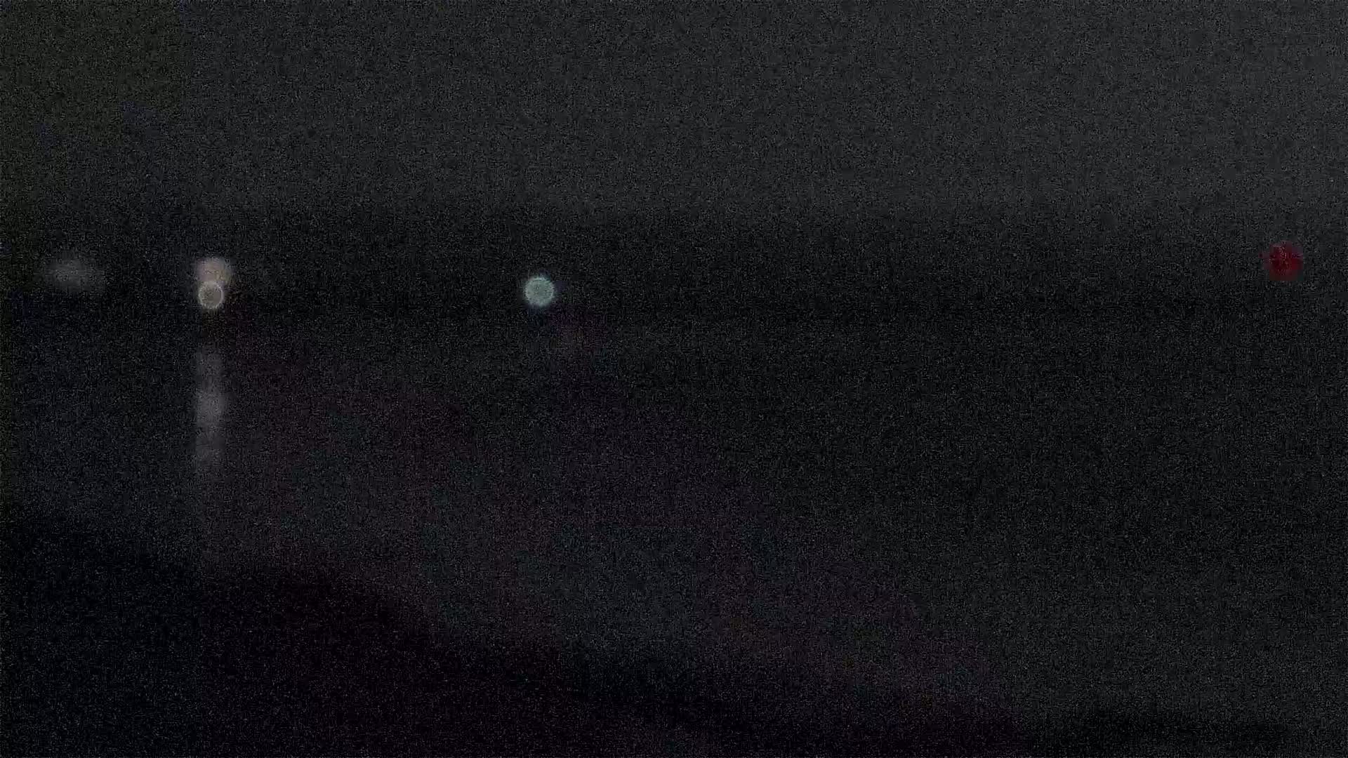 A dark, blurry nighttime scene shows a few out-of-focus lights in the distance.
