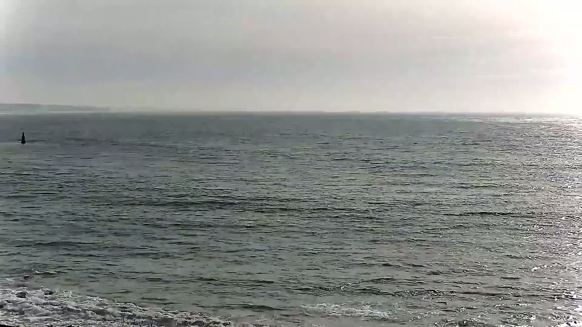 A dark, calm sea stretches to a hazy horizon under an overcast sky, with small waves breaking on the shore in the foreground.