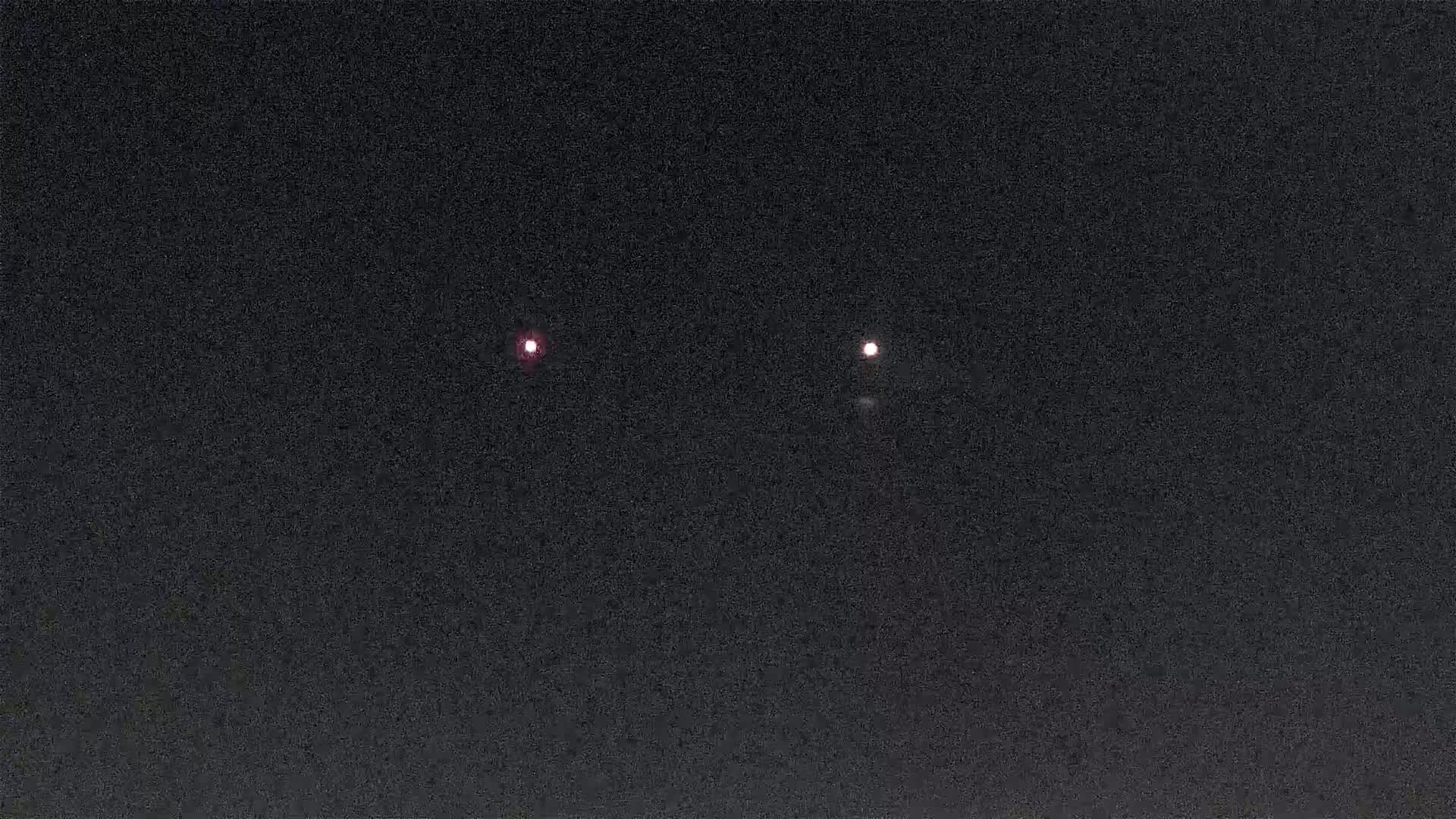 Two faint, reddish lights are visible in a dark, night sky.
