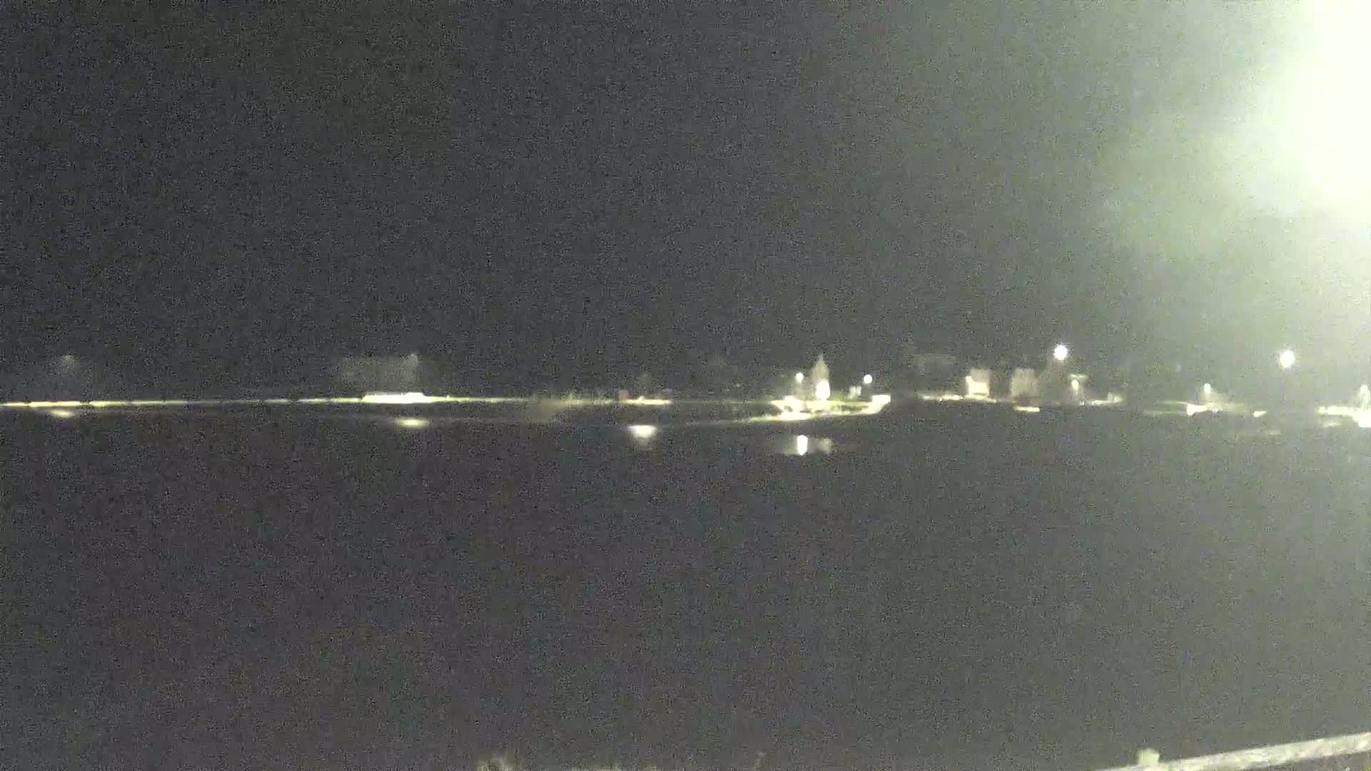 At night, a body of dark water reflects the faint lights of a distant shoreline.