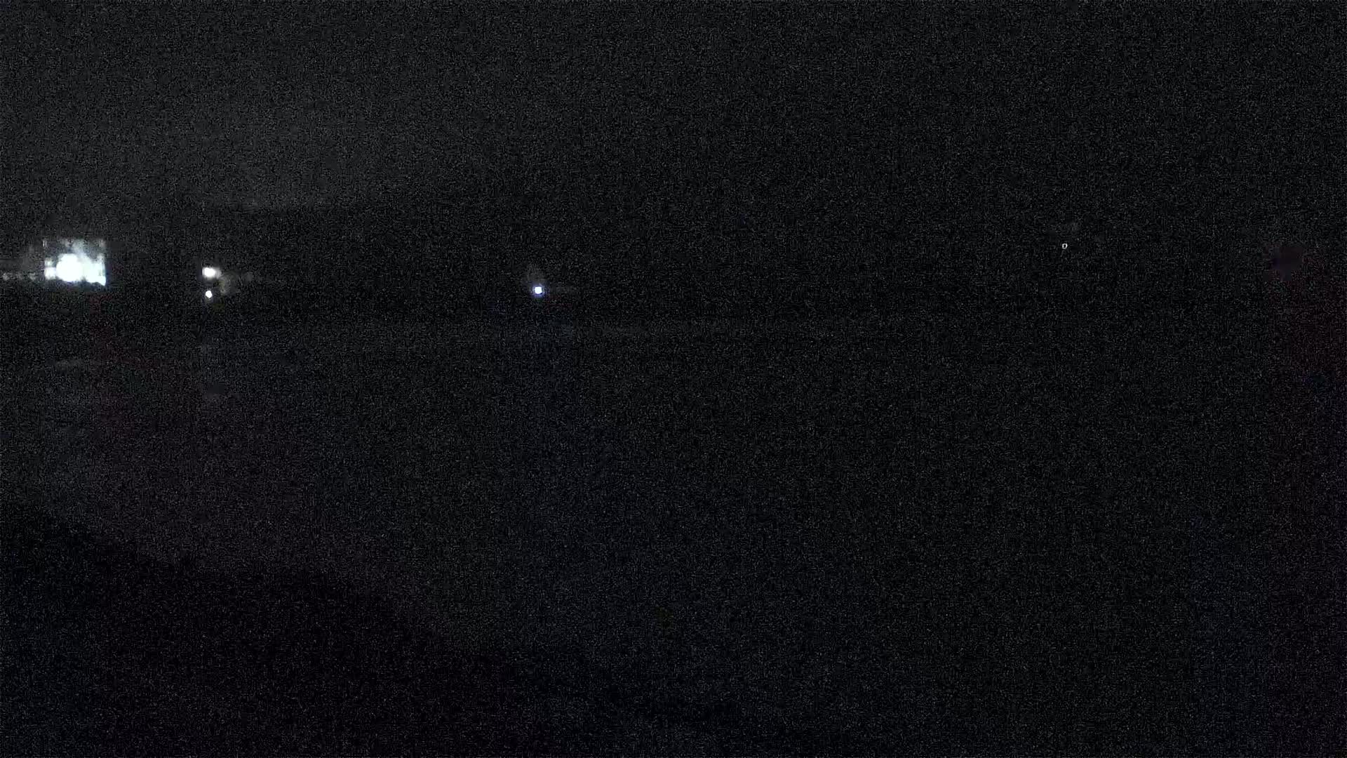 A dark, nighttime scene shows a few distant lights against a mostly black background.