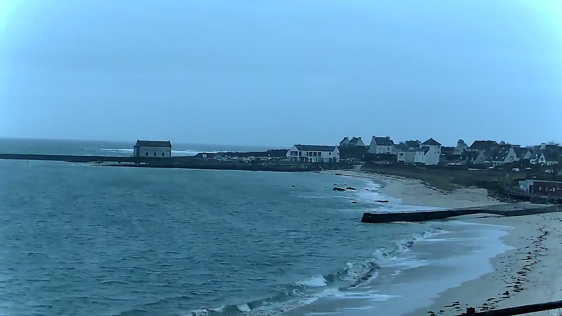 A coastal town with a sandy beach and small waves under an overcast sky.
