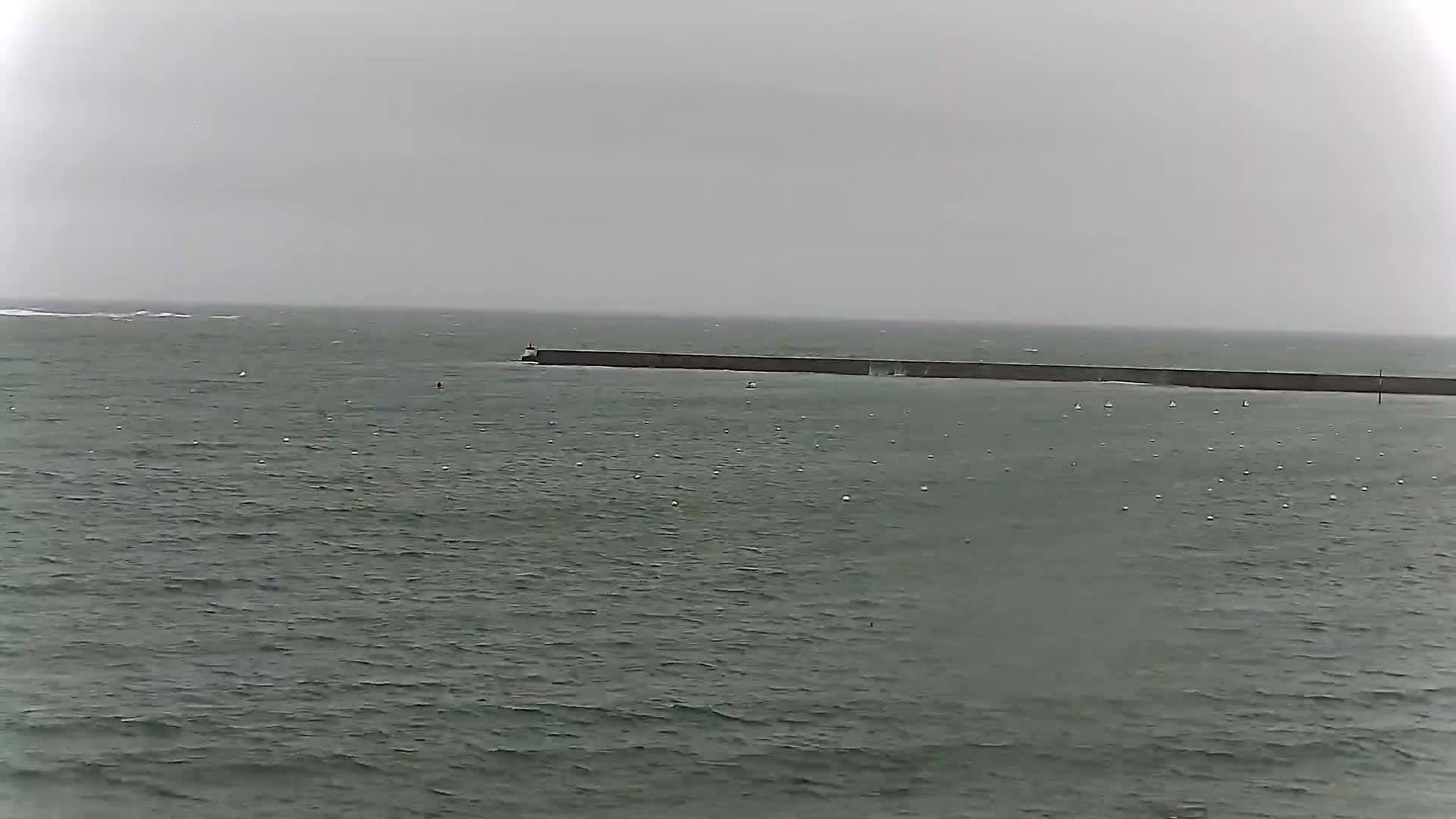 A long, dark breakwater extends across a choppy, gray sea under an overcast sky.