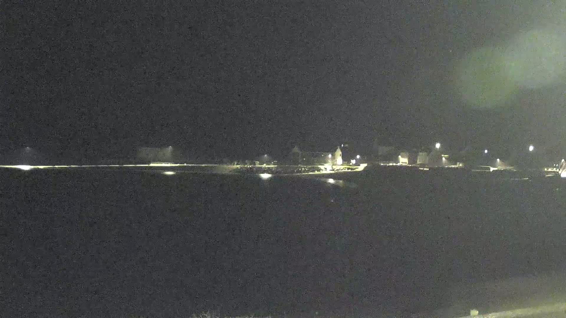 A dark, nighttime scene shows a dimly lit waterfront area with buildings and scattered lights.