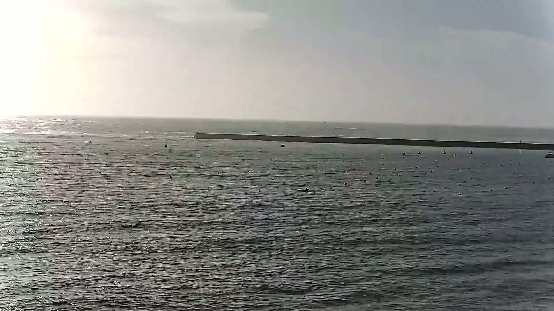 A long, low breakwater stretches across a calm, gray sea under an overcast sky.