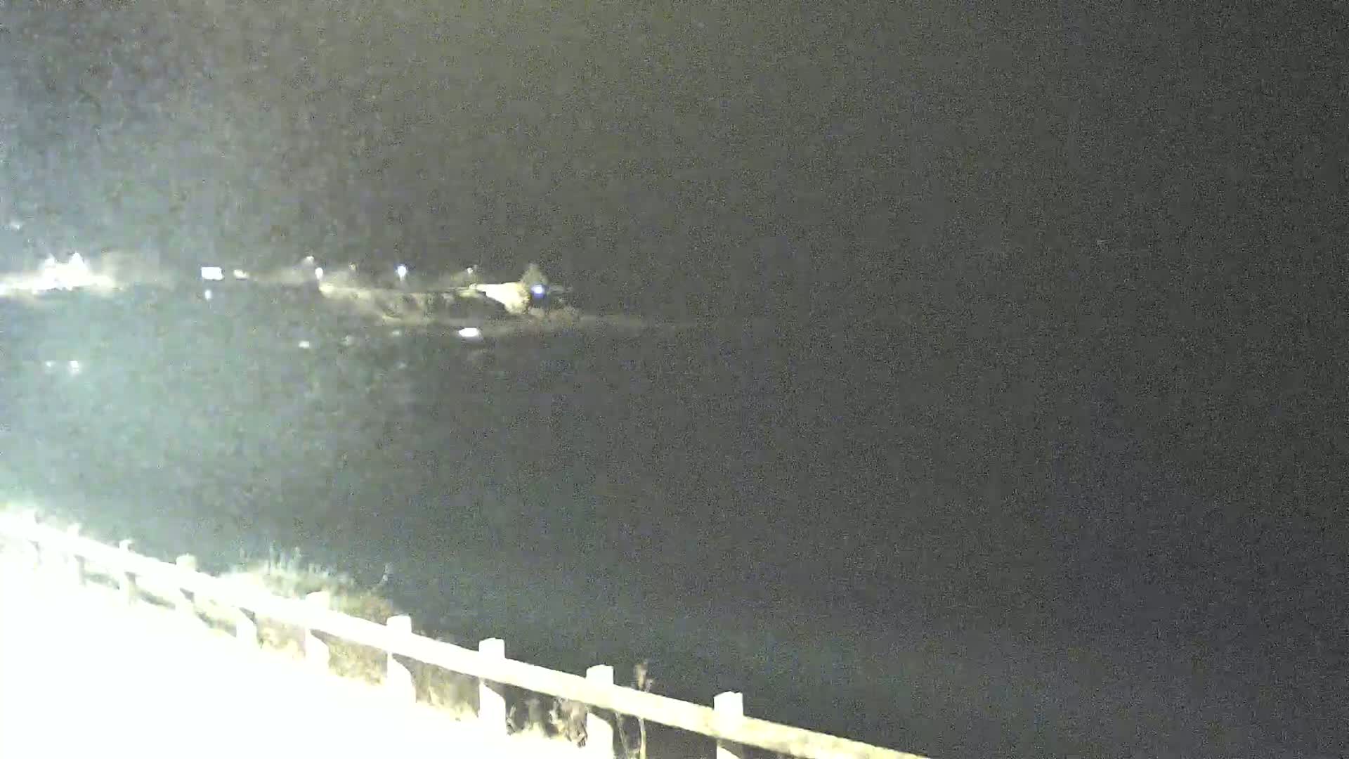 A nighttime, low-light view shows a dark body of water extending from a shoreline with a low fence.