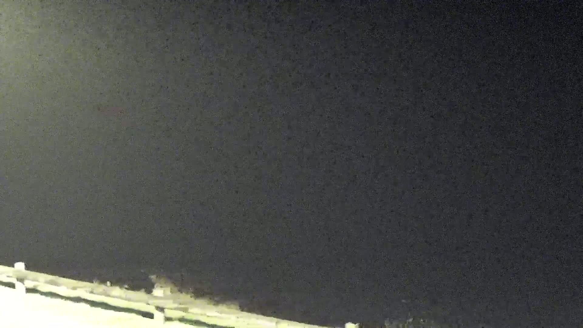 A low-light nighttime view shows a dark sky and a portion of a white railing or fence at the bottom of the frame.