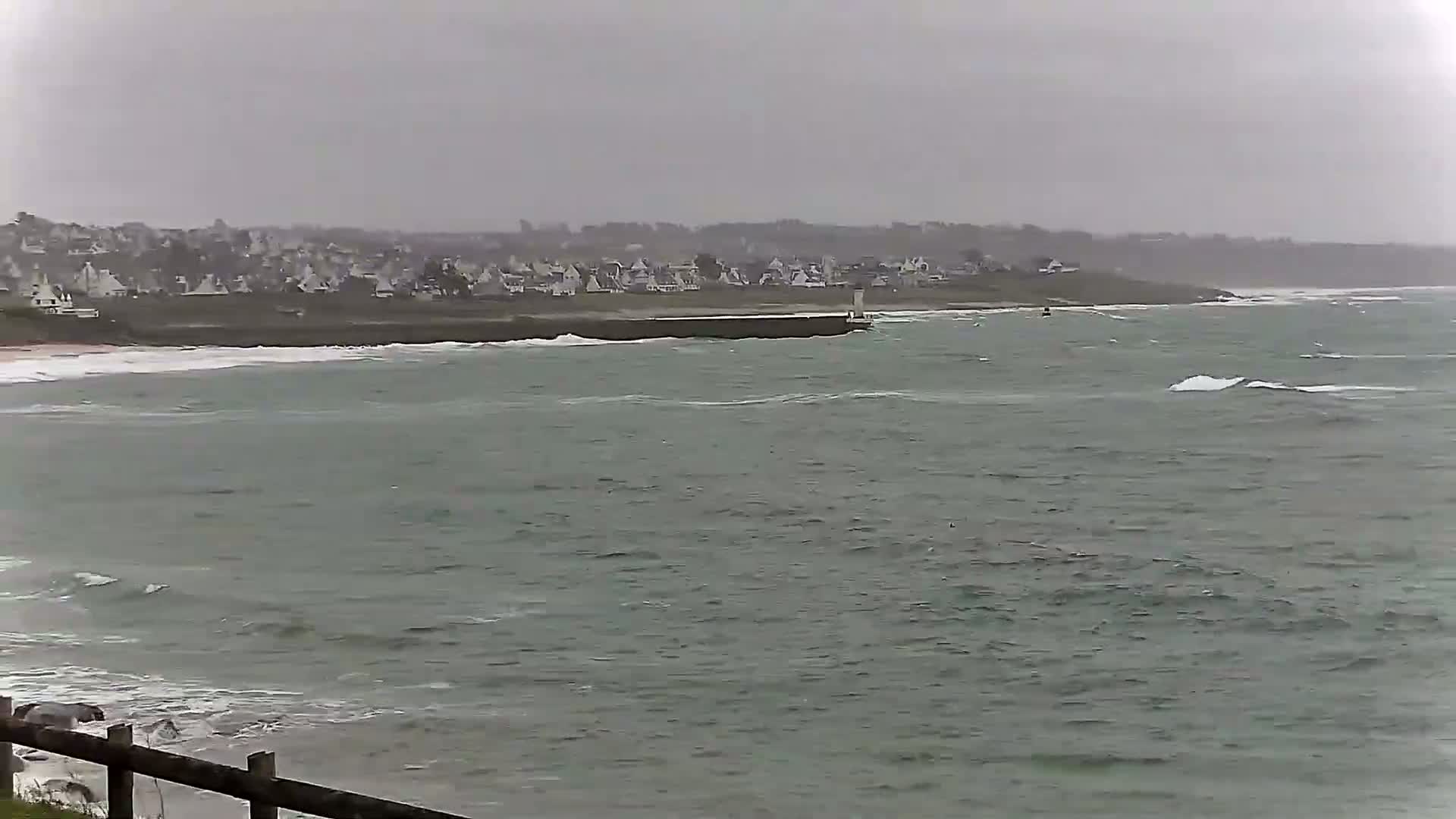 A coastal town is visible in the distance across a choppy sea under an overcast sky.