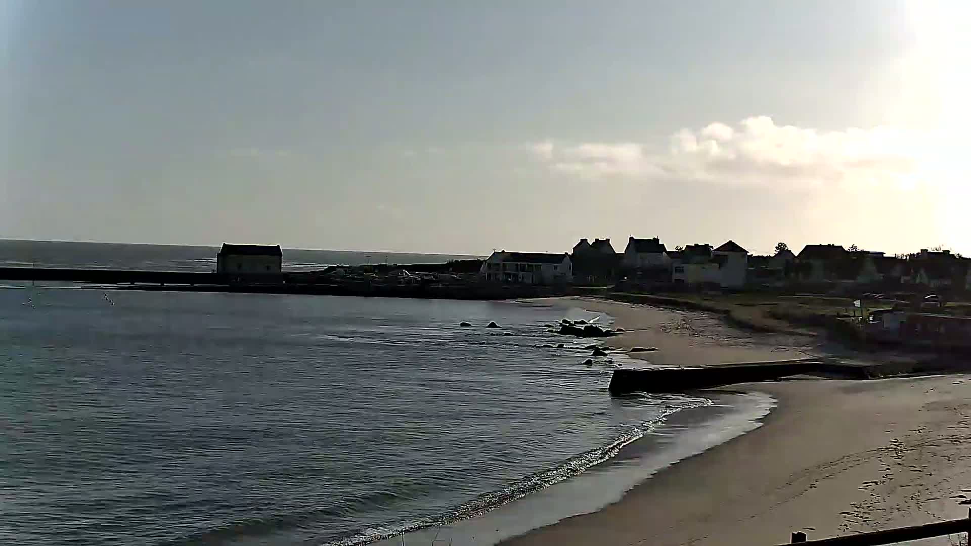 A small coastal town with a sandy beach and calm ocean under a partly cloudy sky.