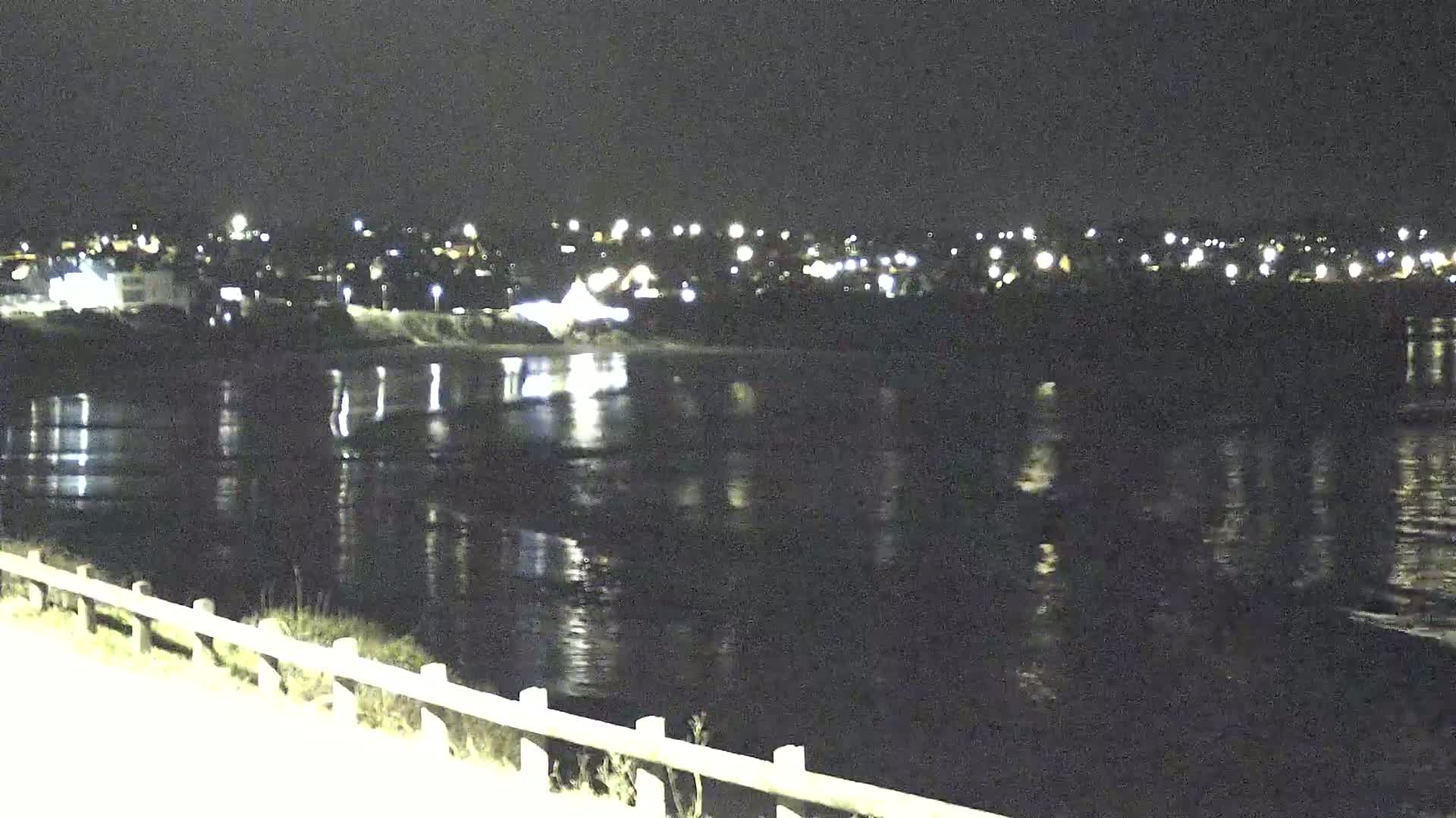 A dark, calm body of water reflects the lights of a distant town at night.