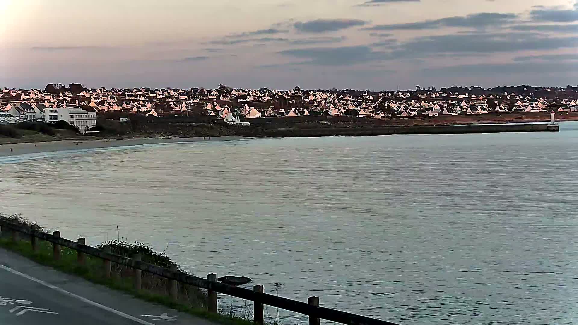 A calm body of water stretches out to a shoreline with a row of houses under a cloudy, dusky sky.