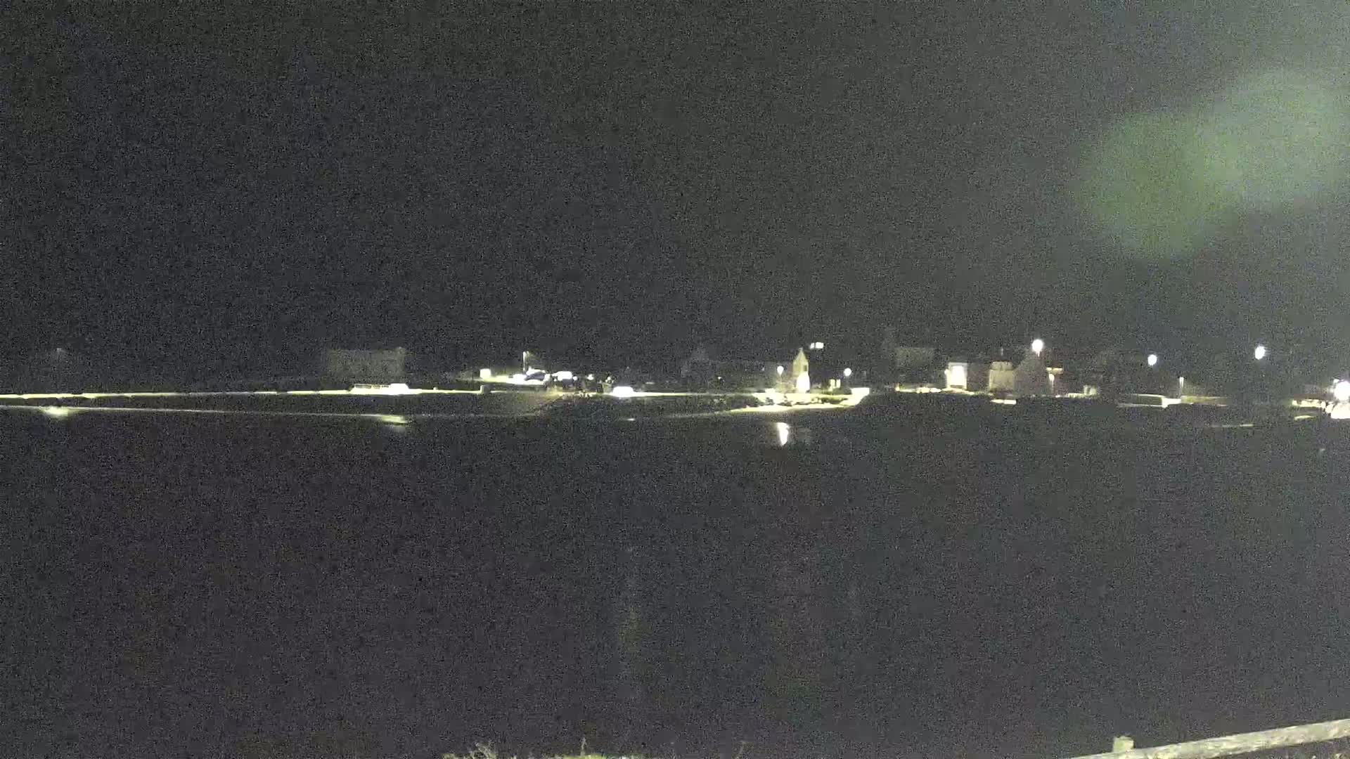 A dimly lit town is visible at night, across a dark body of water.