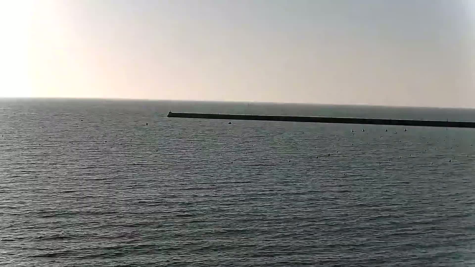 A long, dark breakwater stretches across a calm, gray sea under a pale sky.