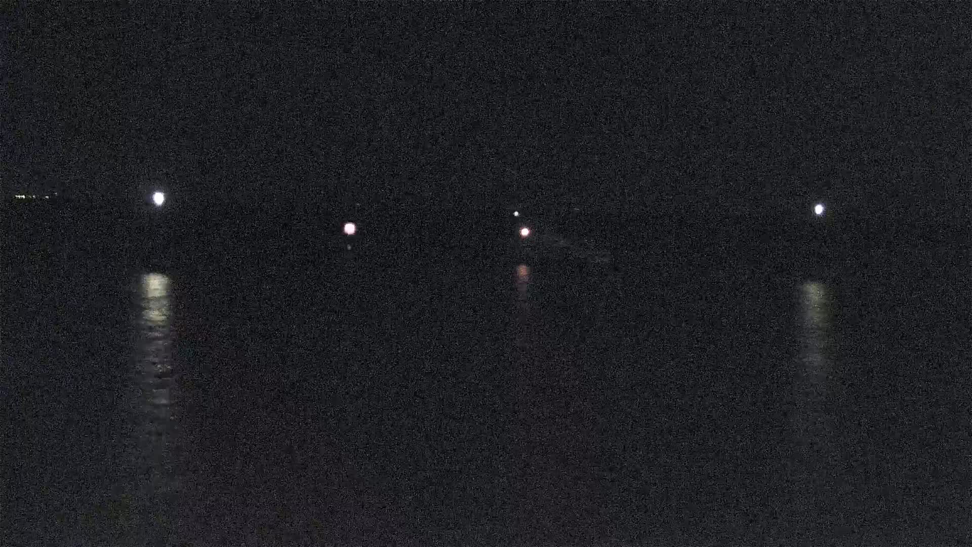At night, several lights are visible across a dark body of water, reflecting on its surface.