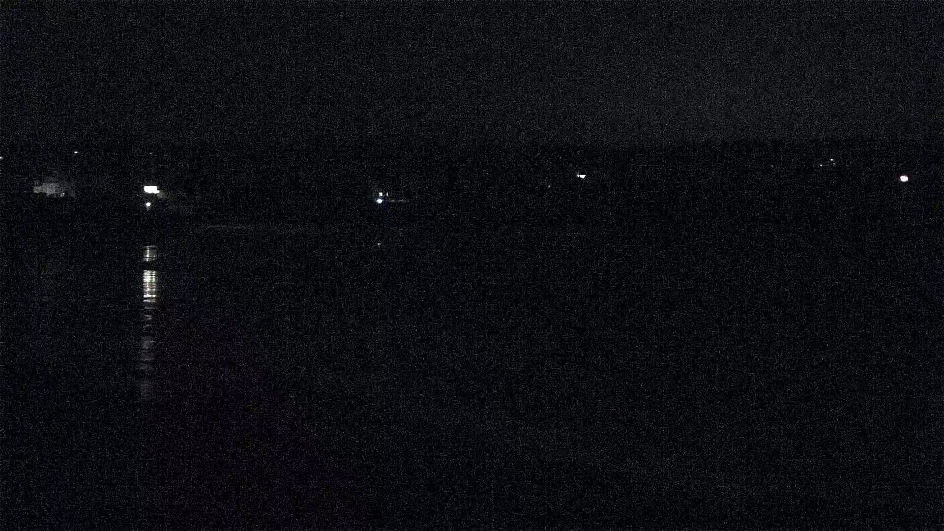 A dark, nighttime scene shows a body of still water reflecting a few distant lights on the far shore.