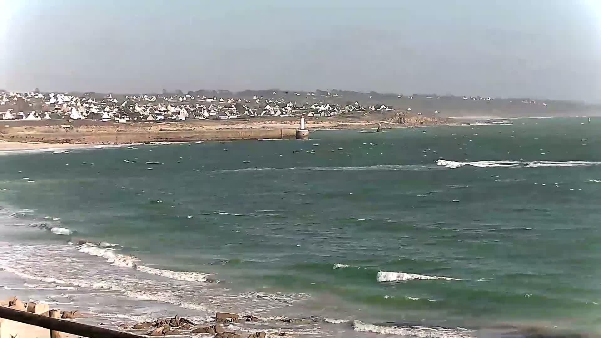 A coastal town is visible across a body of water with small waves under a hazy sky.