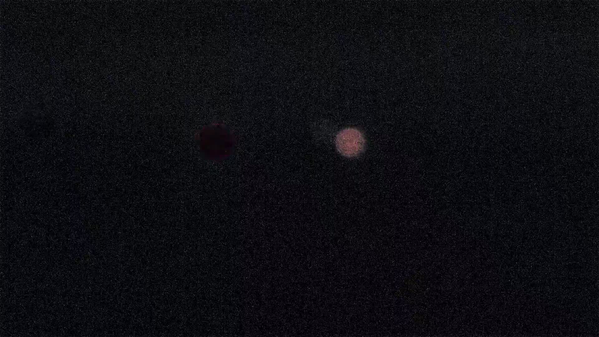 Two blurry, reddish-pink lights appear against a dark, grainy background.