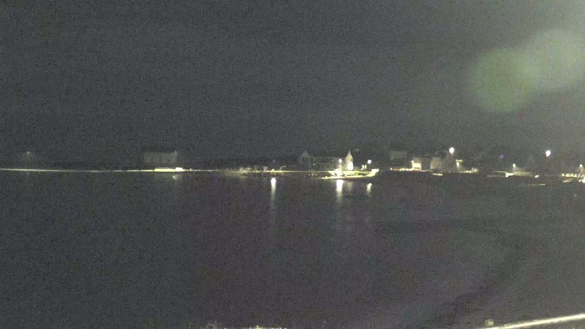 A nighttime view of a calm body of water reflecting the lights of a town across the shore.