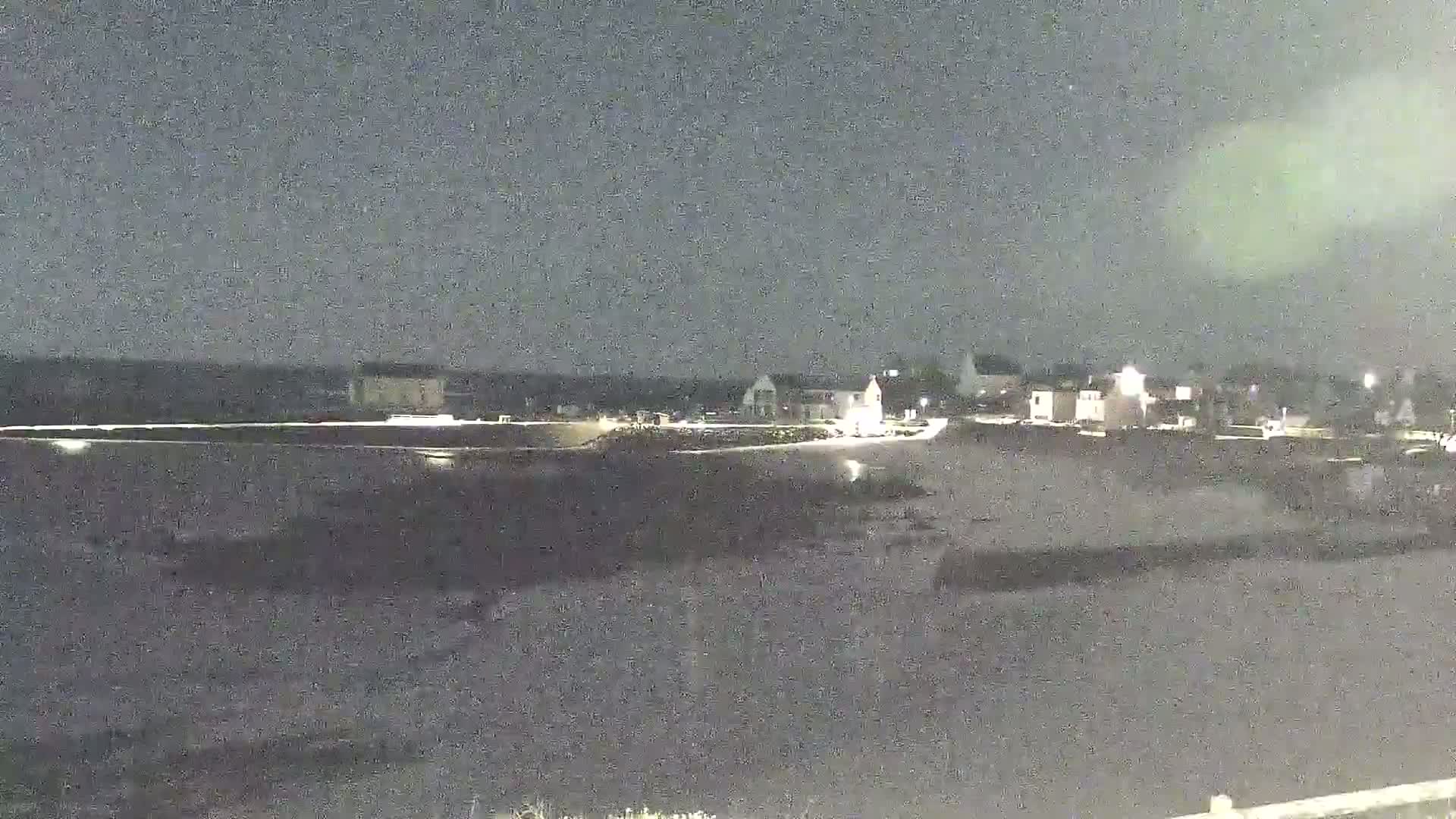 A nighttime, low-light view of a small town or village near a dark body of water under a cloudy sky.