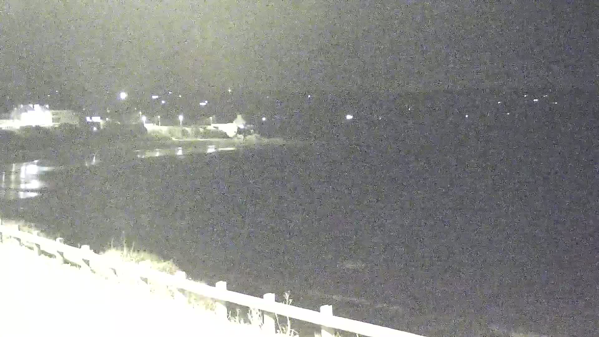 At night, a body of dark water reflects a few distant lights from buildings across the shore, observed from a slightly elevated vantage point with a low railing in the foreground.