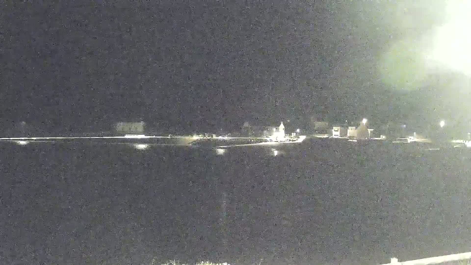 A nighttime, long shot shows a dark body of water reflecting the lights of a small town across its shore.