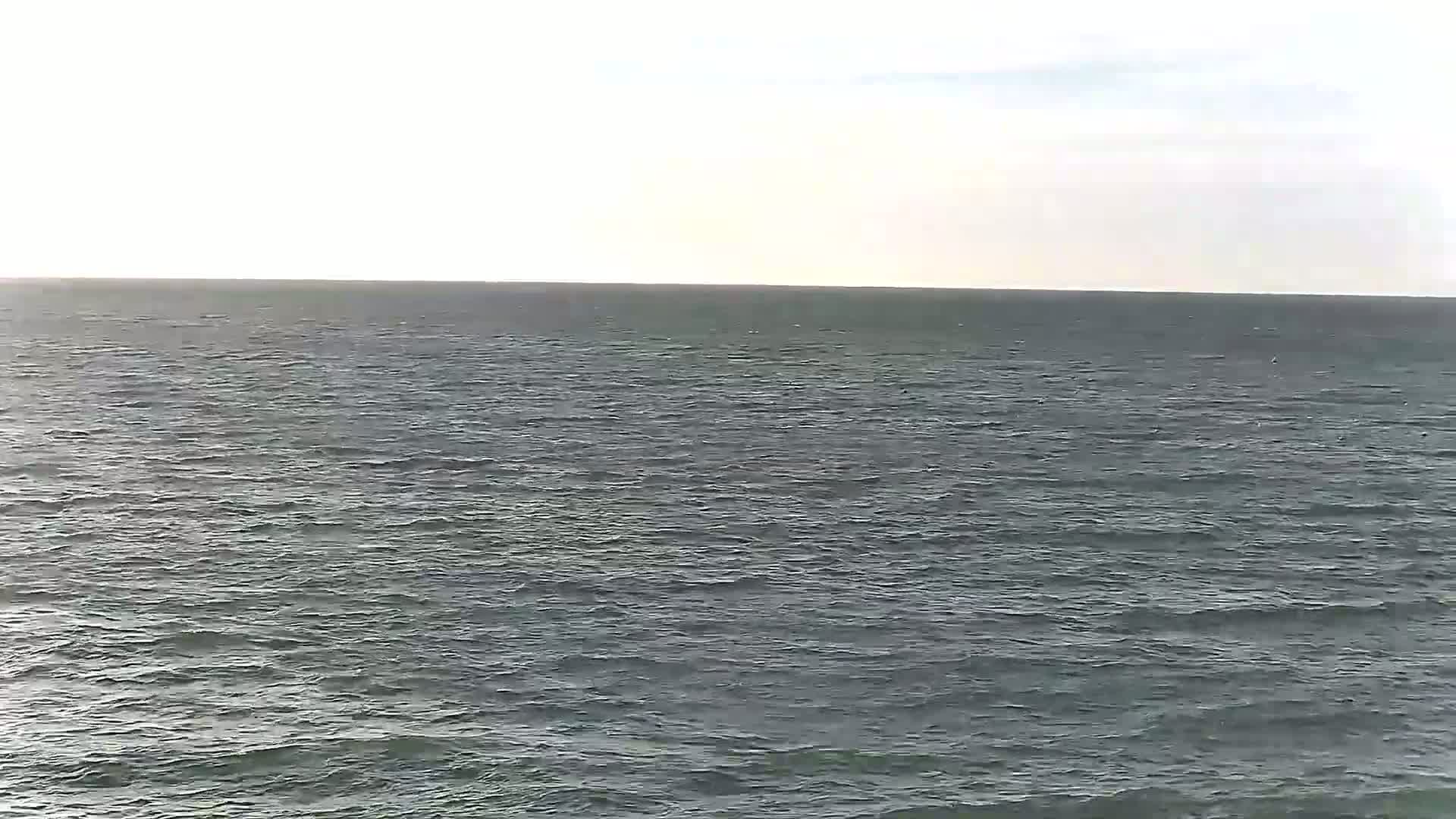 A gently rippling sea stretches to a pale sky under mostly clear conditions.