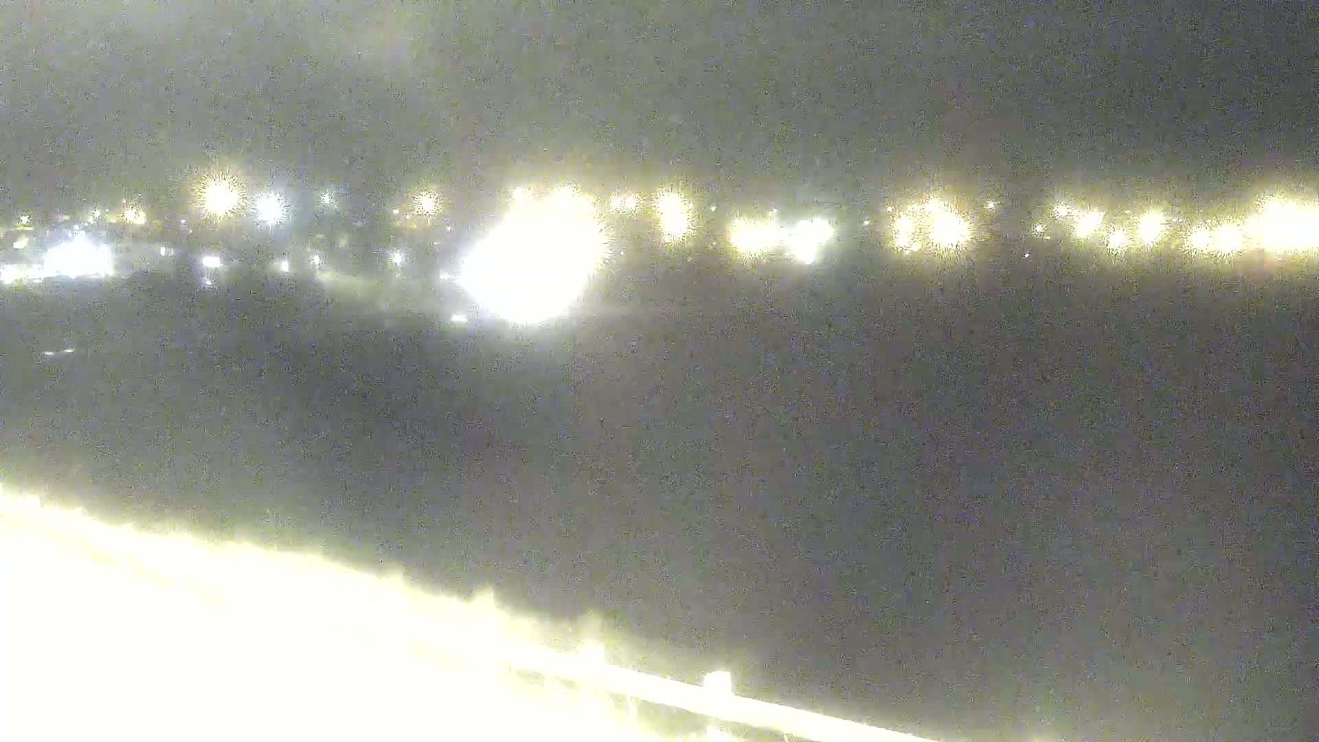 A nighttime view shows a blurry line of distant lights across the horizon under a dark, cloudy sky.