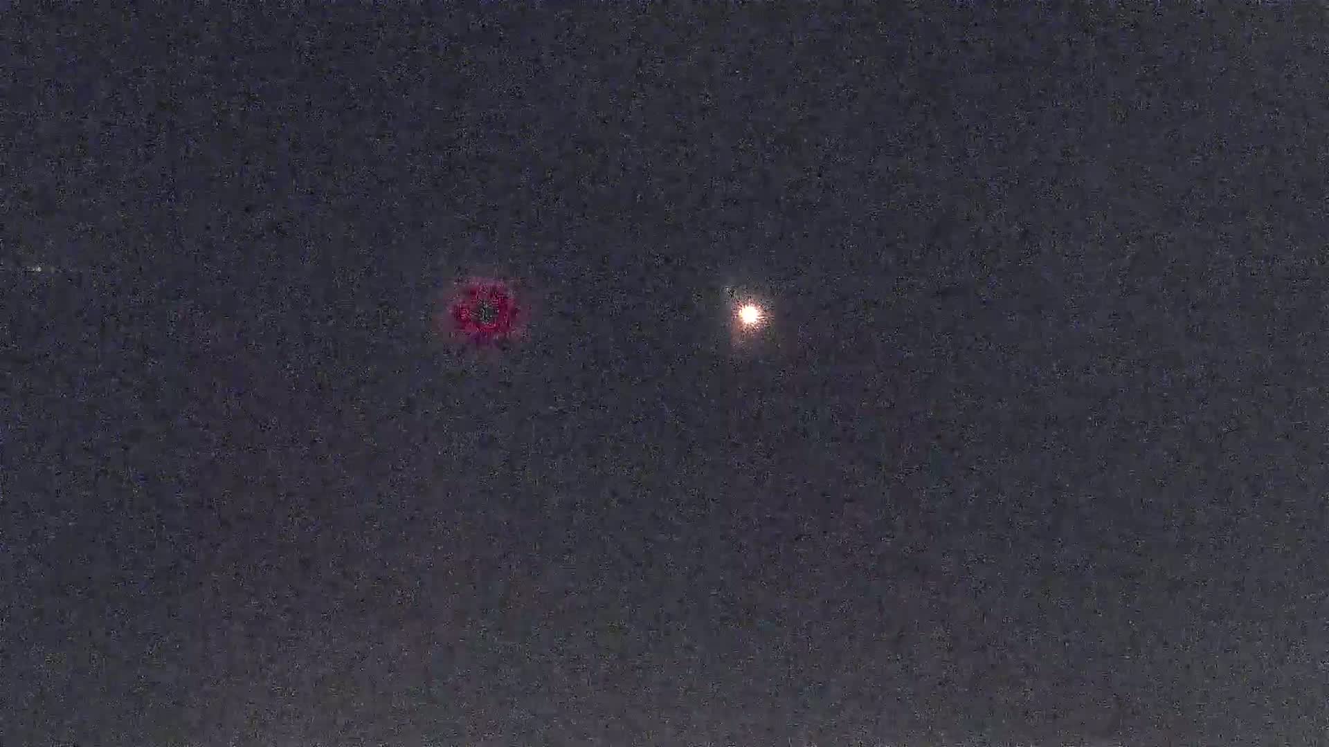 A dark night sky shows two bright lights, one reddish and one yellowish-white.