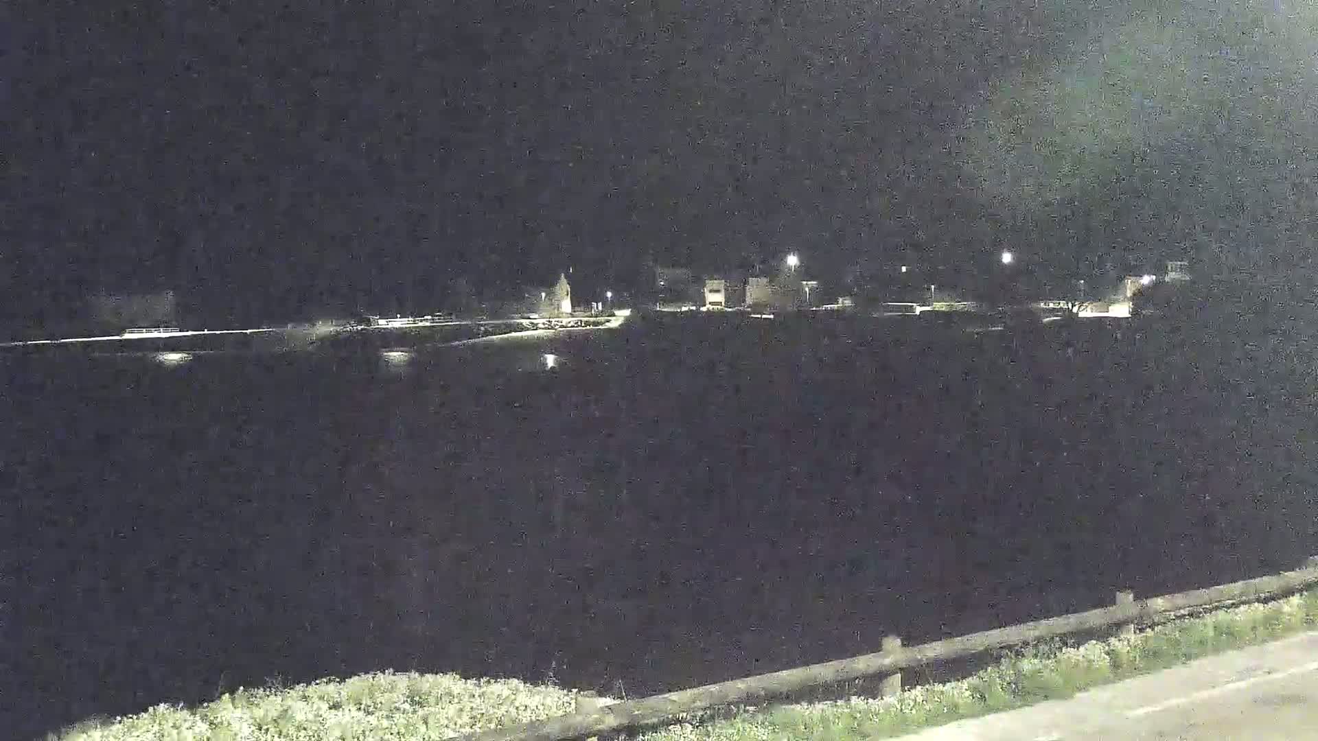 A nighttime view of a dark body of water reflecting a few lights from buildings in the distance.