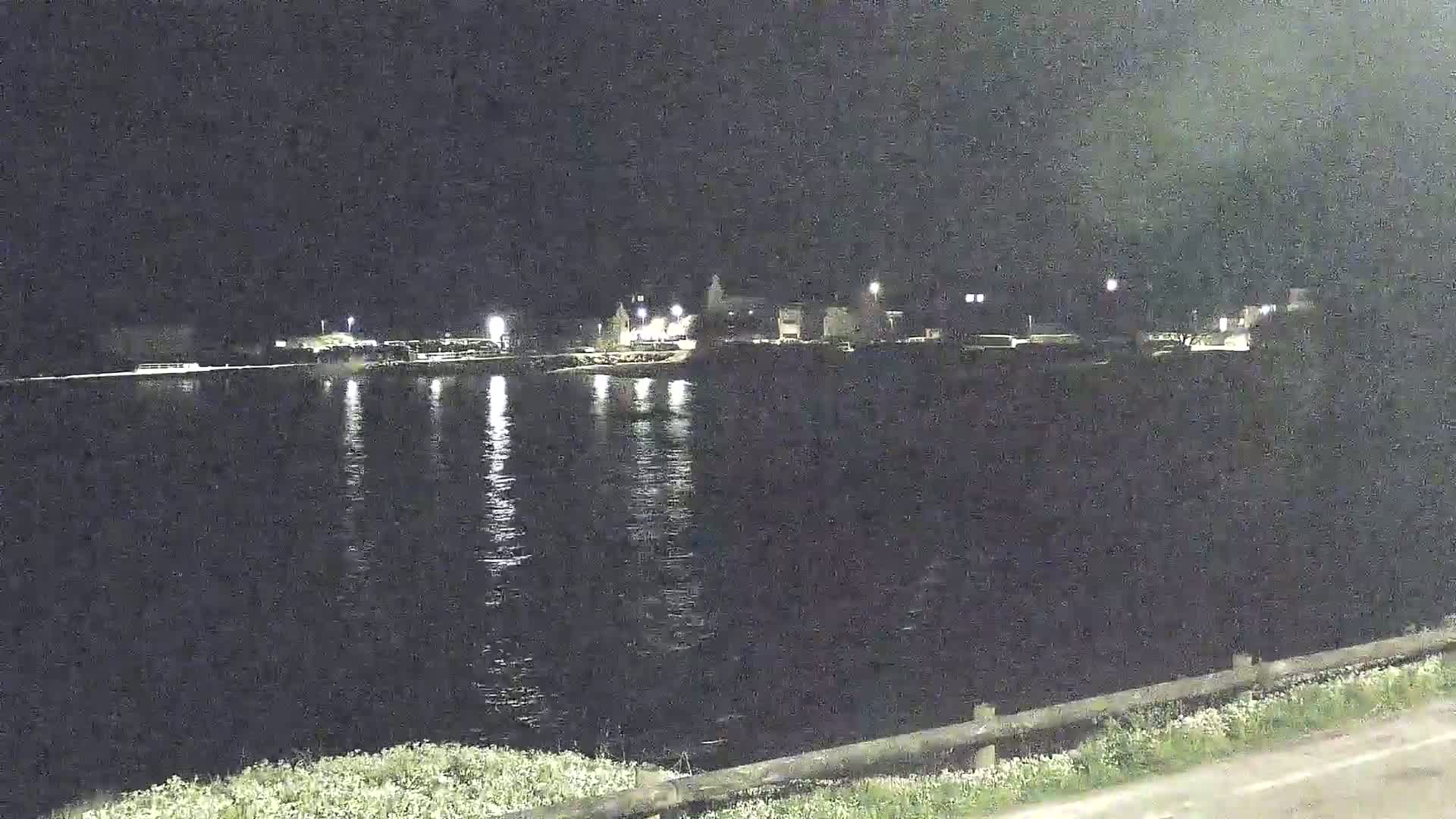A nighttime view of a calm body of water reflecting the lights of a town across the water.