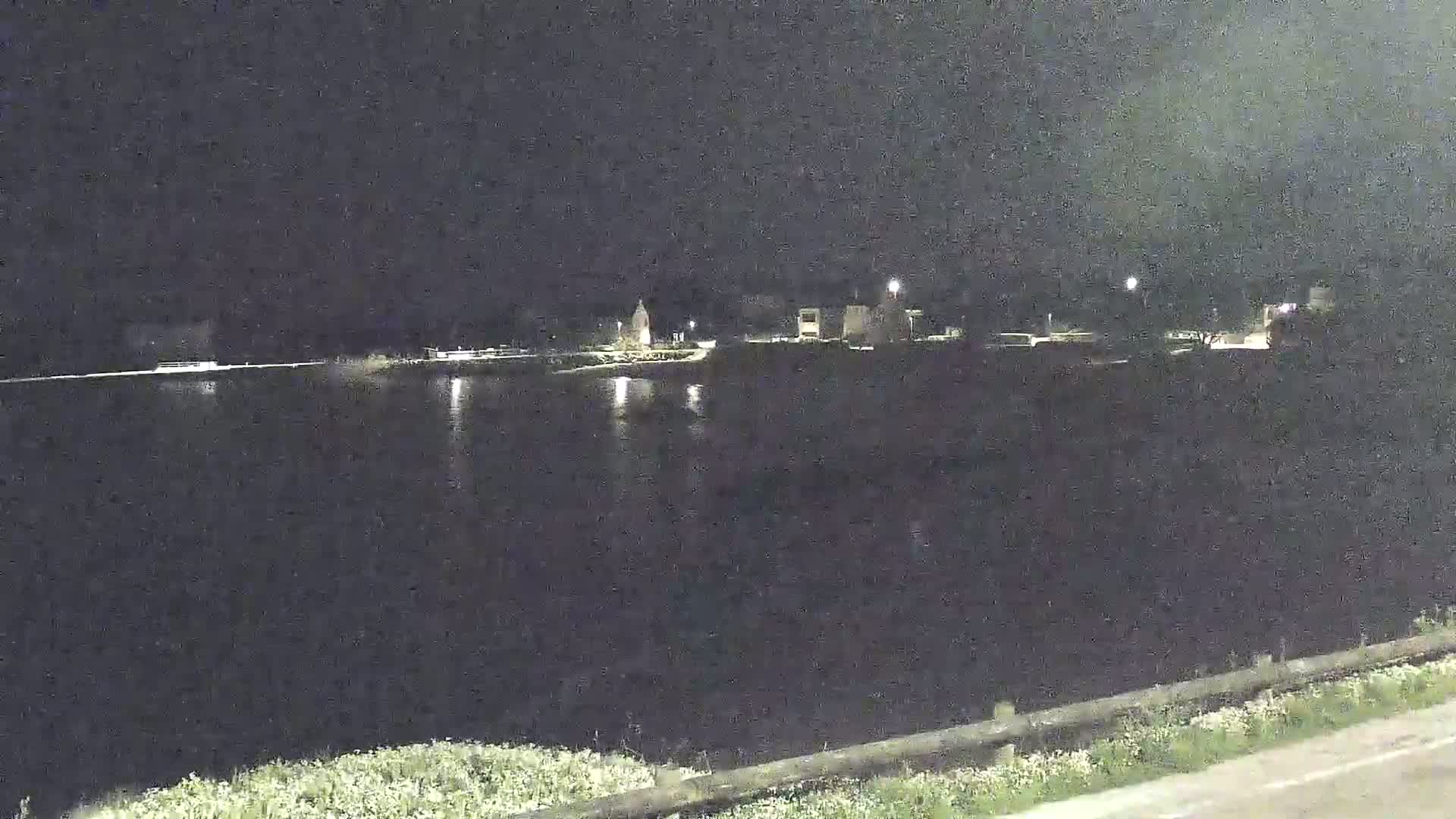 A dark body of water reflects the faint lights of a distant, dimly lit town at night.