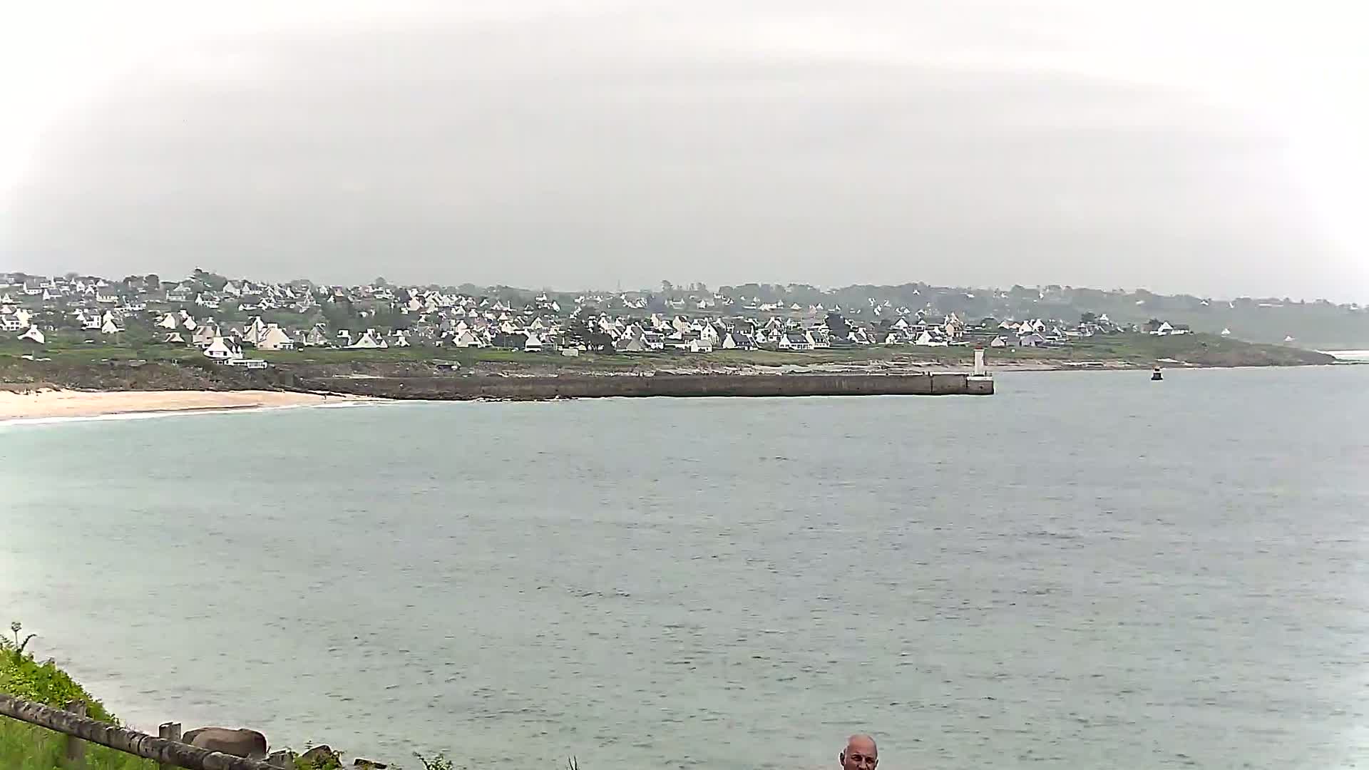 A coastal town with white houses sits behind a calm, gray ocean on an overcast day.