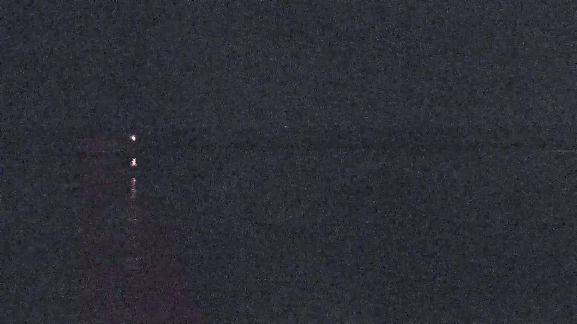 The image shows three faint lights reflected on dark water at night.