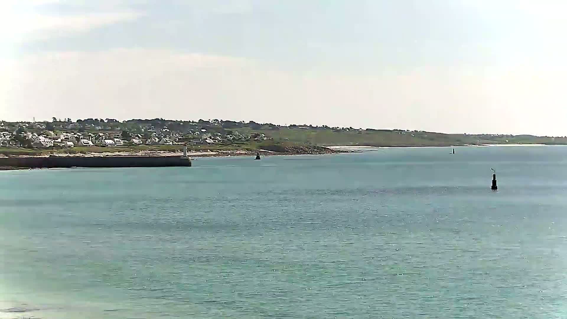 A calm, light-blue body of water stretches out to a distant coastline featuring a small town under a partly cloudy sky.