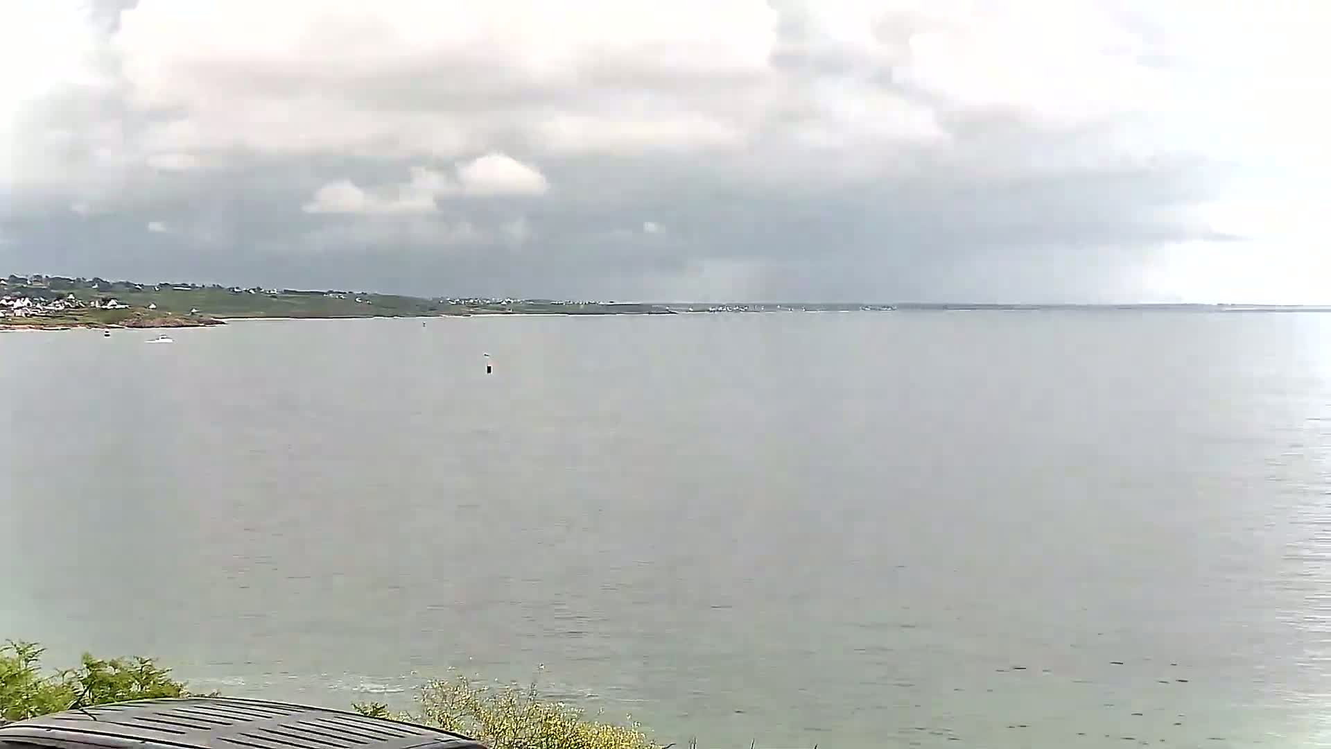 A calm body of water stretches to a distant shoreline under a cloudy sky.