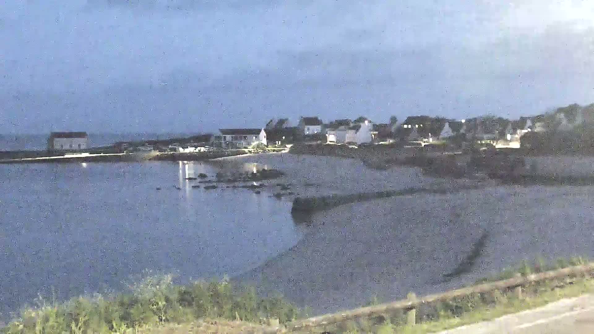 A small coastal village is visible at dusk, with calm water reflecting the dim light.