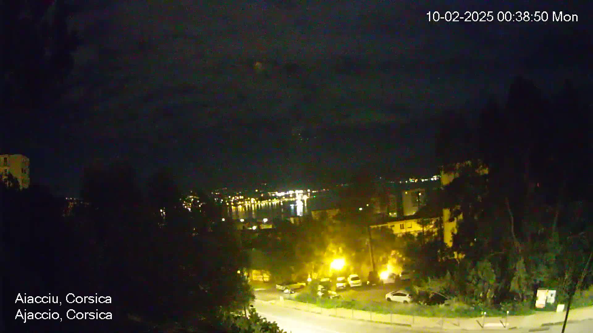 A nighttime view of a city with a body of water in the distance under a slightly cloudy sky.