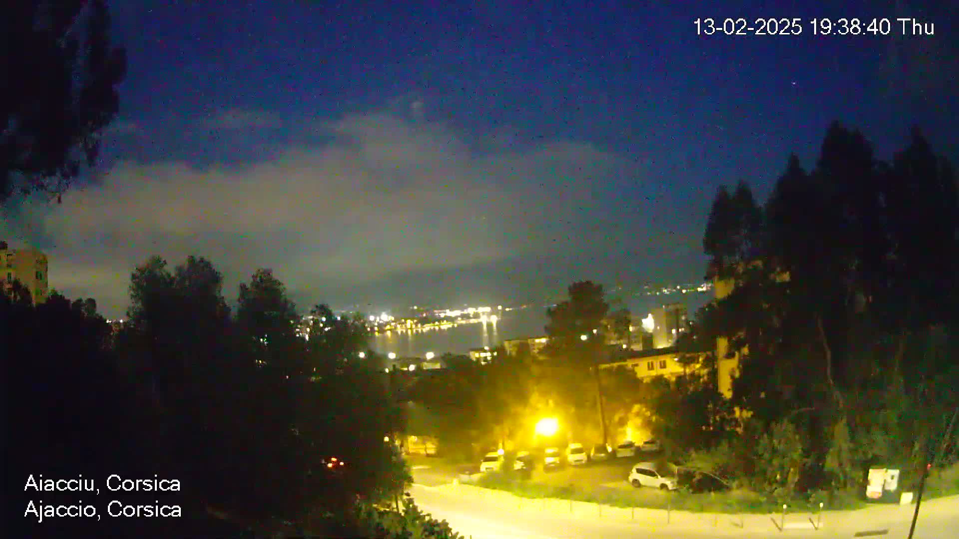 A nighttime view of a city overlooking a body of water under a mostly clear, dark sky with some light cloud cover.