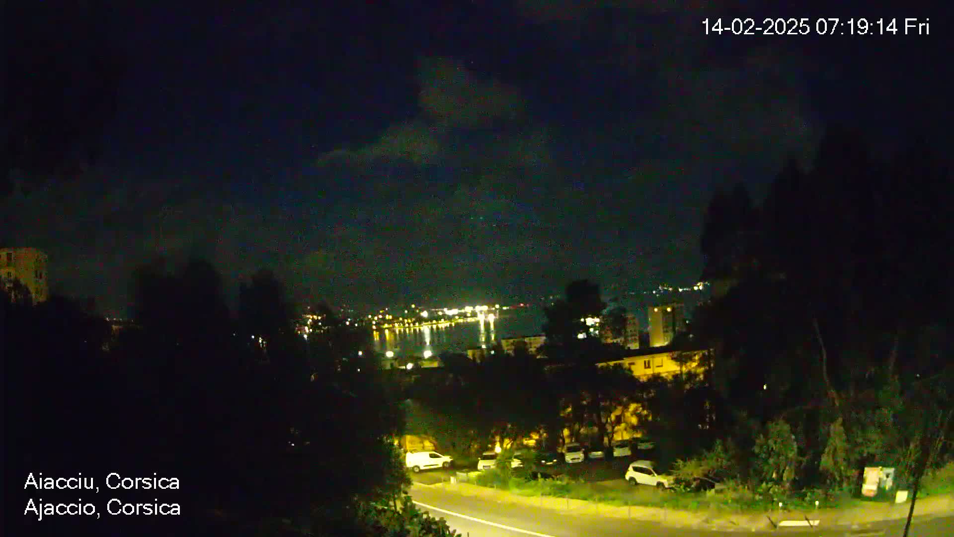 A nighttime view of a city overlooking a body of water under a partly cloudy sky.