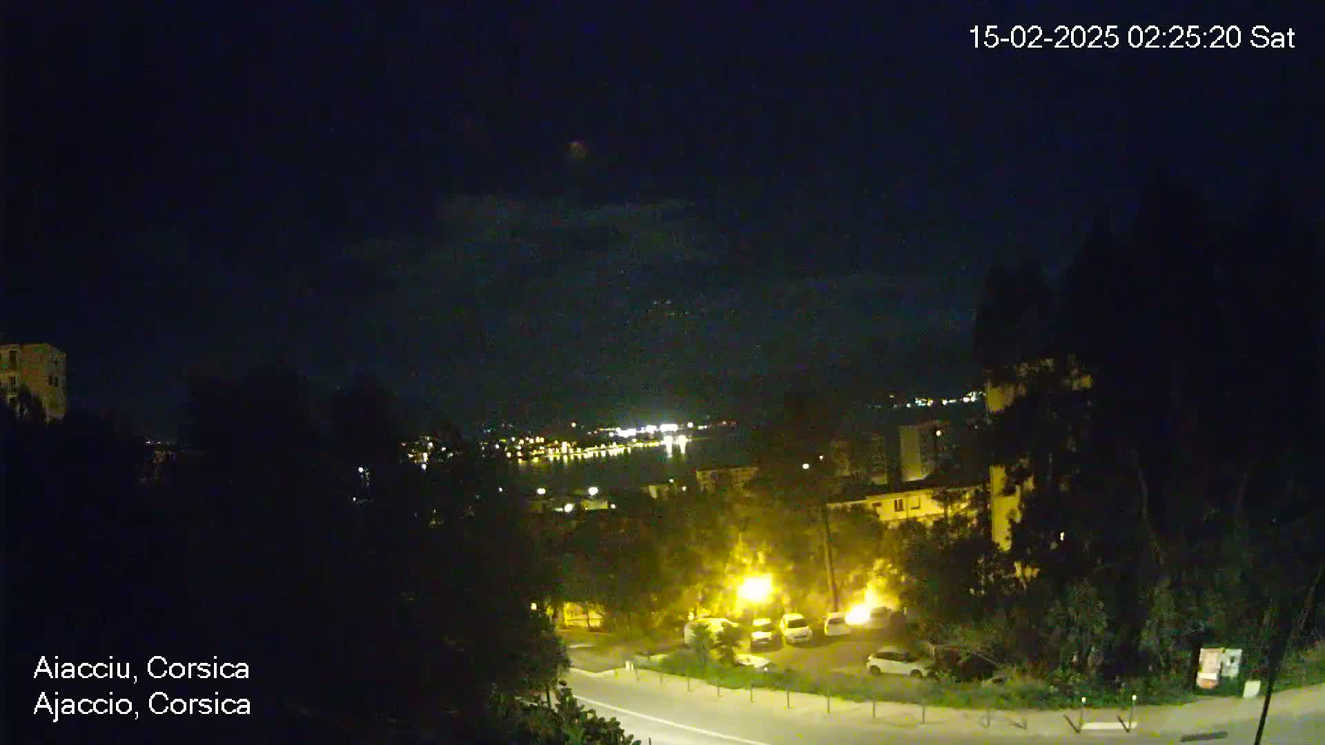 A nighttime view of a city near a body of water, under a clear sky with a few lights visible on the water and in the city.