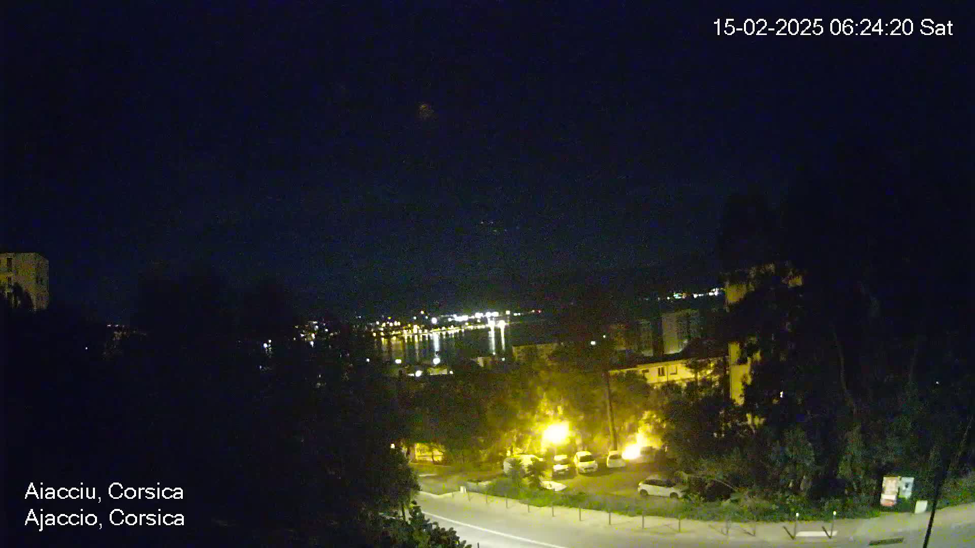 A nighttime view of a coastal town, with a body of water and lights visible in the distance under a clear, dark sky.
