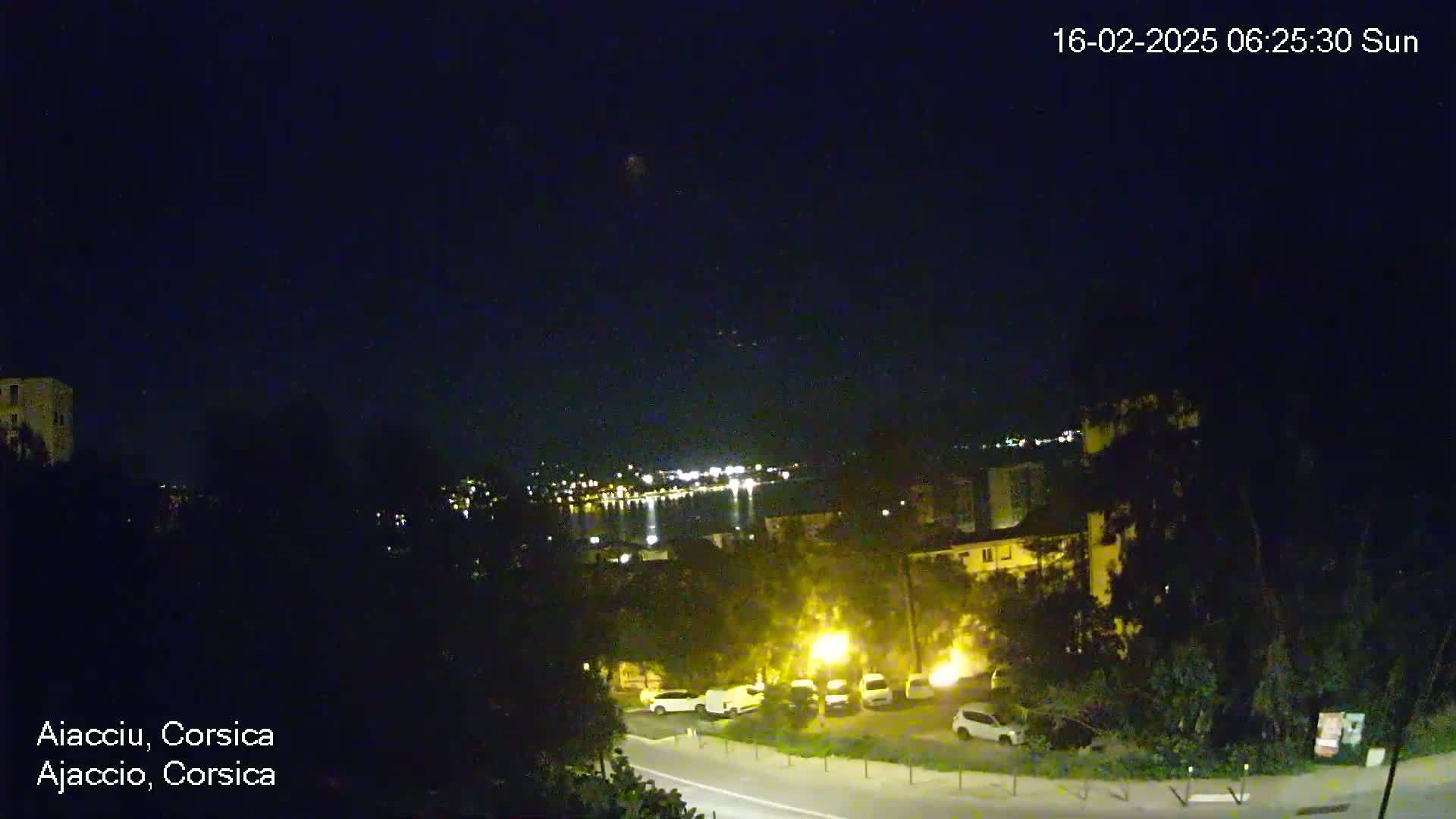 A nighttime view of a city along a body of water, with dimly lit buildings and cars visible under a clear, dark sky.