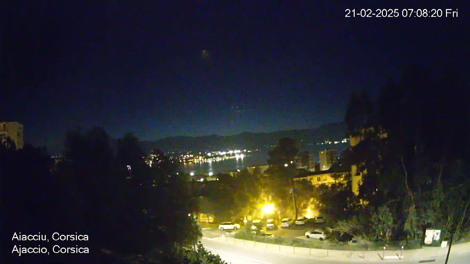A nighttime view of a city by the water, with hills in the background under a clear, dark sky.
