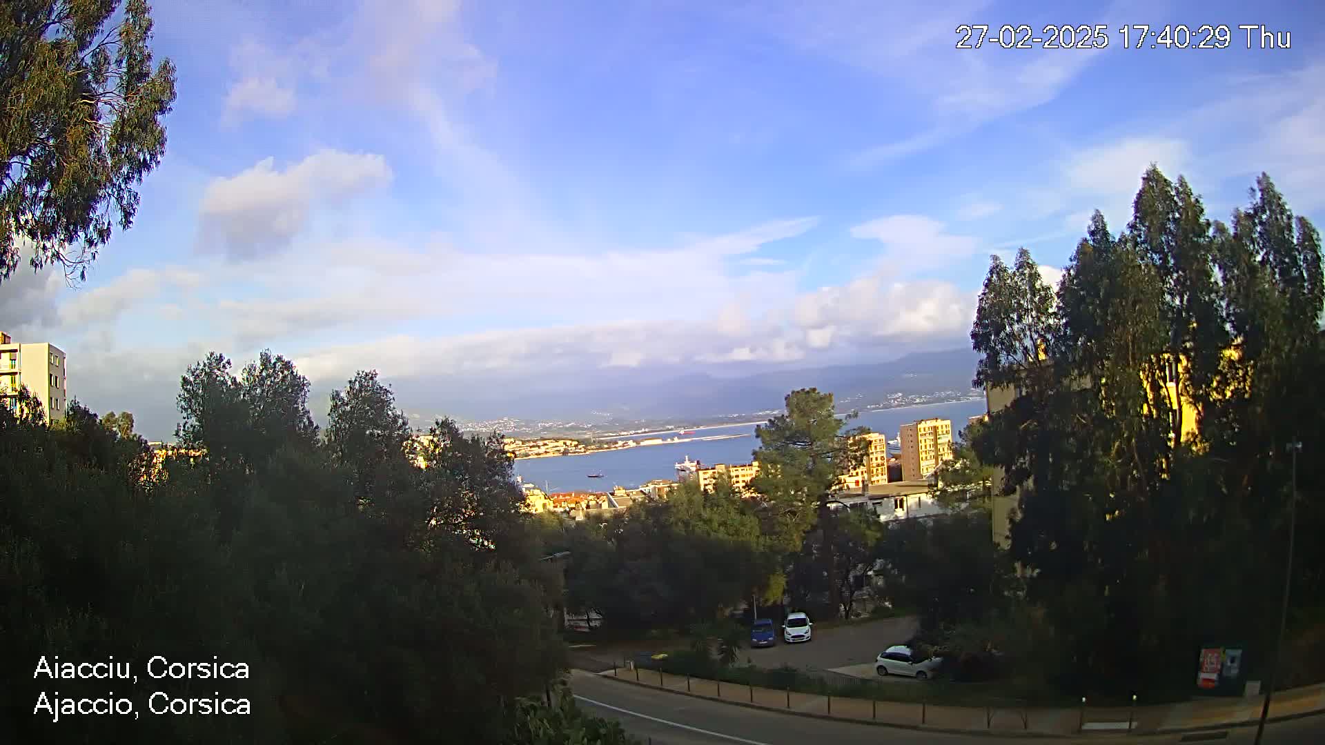 A partly cloudy daytime view overlooking a city, a body of water, and distant mountains.