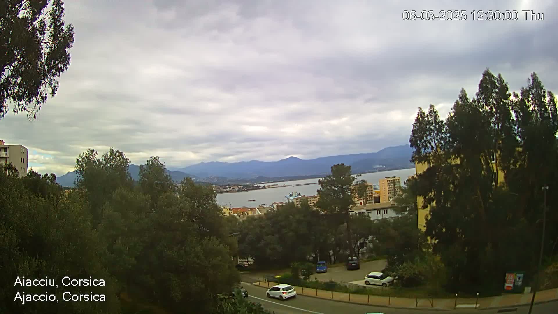 A view of a city and harbor nestled between mountains under a cloudy sky.
