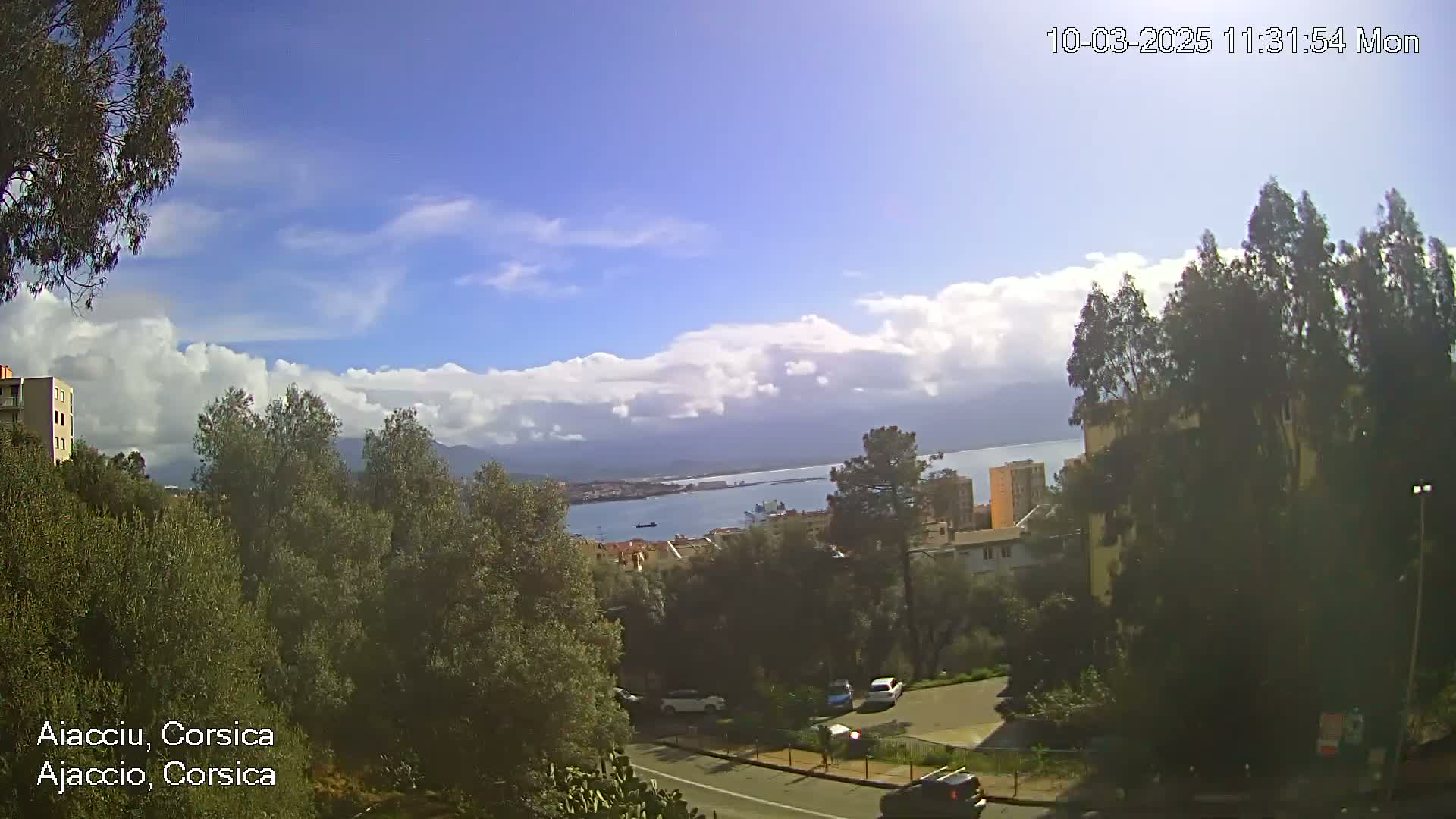 A partly cloudy day overlooks a city with a body of water and mountains in the distance.