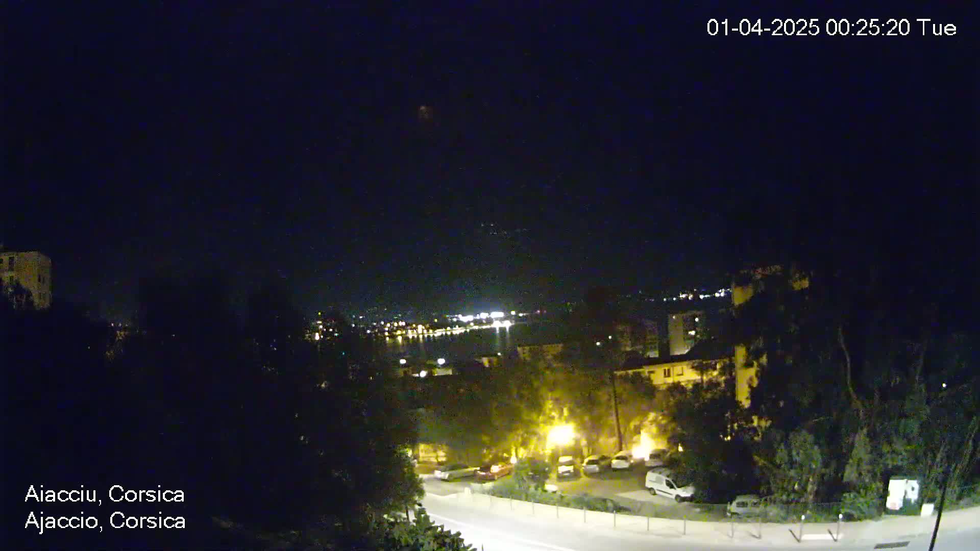 A nighttime view of a coastal town with a body of water in the background under a clear, dark sky.
